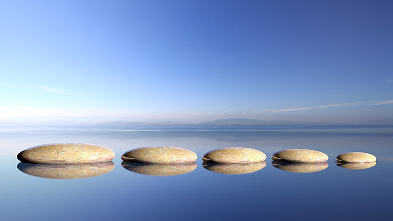 Zen stones row from large to small in water with blue sky and p